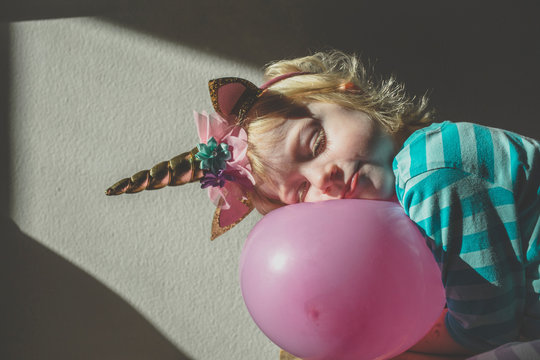 Portrait of little blond girl wearing unicorn horn leaning on pink balloon
