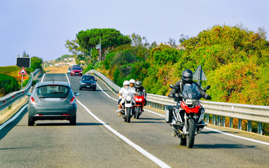 Bicycles and car on road at in Sardinia Island in Italy in summer. Bikers driving scooter on highway of Europe. Men riding bikes on motorway. Olbia province. Mixed media.