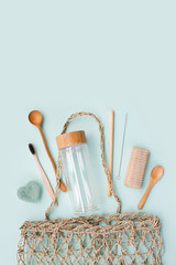 Natural accessories: luffa washcloth, bamboo toothbrush, glass drink bottle with bamboo cover, bamboo straw with metal brush, wooden comb and spoon in wicker shopping bag.