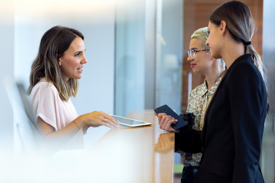 Two businesswomen talking to woman at reception desk