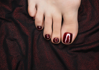 Female toes with beautiful bloody red glossy pedicure on the drape of dark shiny fabric, close up....