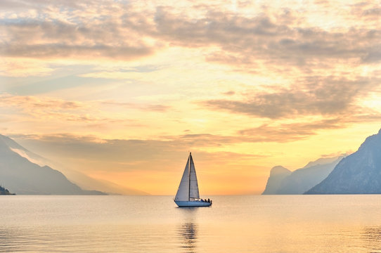 Italy, Trentino, Nago-Torbole, Sailboat sailing near coastal cliffs of Lake Garda at moody dawn