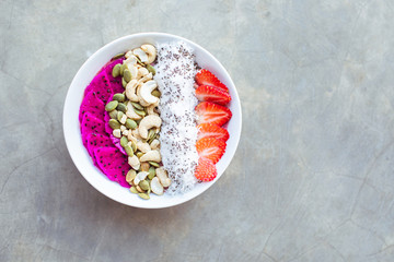Healthy breakfast smoothie bowl topped with pitaya, cashew, coconut flakes and strawberry on gray background. Copy space.