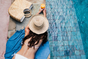Young woman in straw hat relaxing on the swimming pool with orange detox juice. Summer holiday concept. Top view.