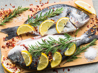 Mediterranean seafood concept. Raw dorado fish with lemon, spices and rosemary on wooden board. Fresh organic sea bream or dorada fish. Top view