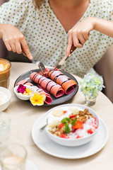 Woman eating delisious pink crispy pancake. It made from pitaya - dragon fruit. Fresh homemade crepes with chocolate sauce on marble table.