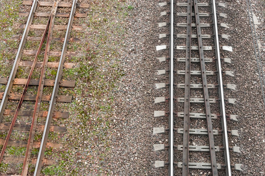 Two parallel railway tracks. top view. On left is old rusty road with wooden sleepers. On right is new shiny one with reinforced concrete support for rails
