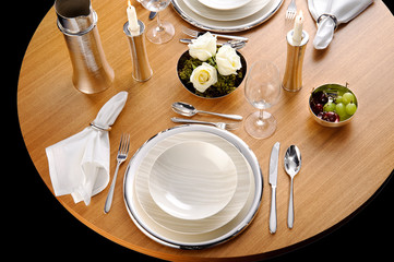 A round table set up with dinnerware and silverware, ready for a meal.