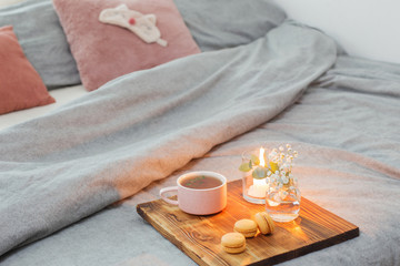 herbal tea with macaroons and candles on wooden tray on bed