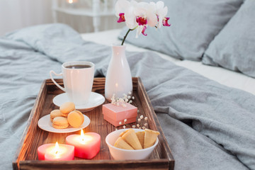 Coffee, sweets,  candles, flowers and girt on wooden tray on bed. Concept with Valentines day