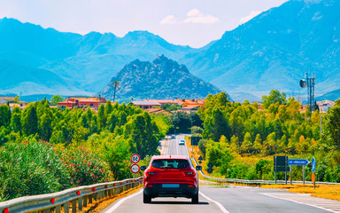 Red Car on the road at Carbonia in Sardinia Island in Italy summer. Transport driving on the highway of Europe. Holiday View on motorway. Cagliari province. Mountains on background. Mixed media.