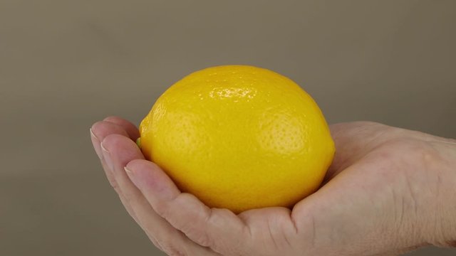 The camera shows a female hand with a lemon from blur to focus, closeup