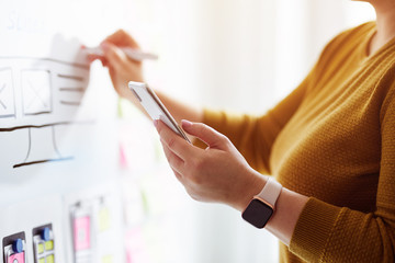 Female web developer with mobile phone and red marker planning website on whiteboard