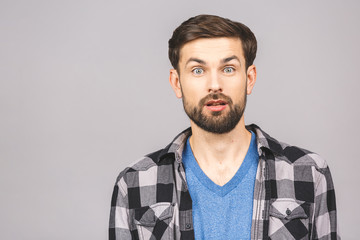 OMG! It's incredible! Portrait of handsome young man looking at camera while standing against isolated grey background. Close up portrait of bearded man keeping his mouth open.