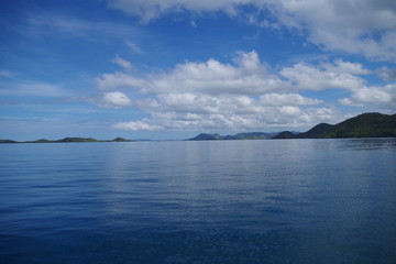 Fototapeta na wymiar A panorama of the Indian Ocean in the Philippines Archipelago. There are several forested islands visible on the horizon. It's a bright summer day - both water and sky are very blue. 