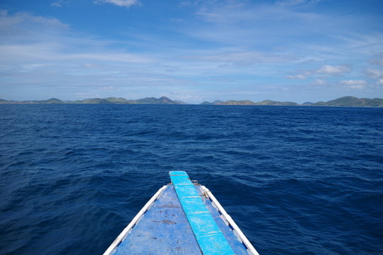 A view from a lone paraw boat sailing the Indian Ocean. On the horizon, many islands can be seen. The water is blue and calm. It's a warm sunny summer day and there are few clouds in the sky.