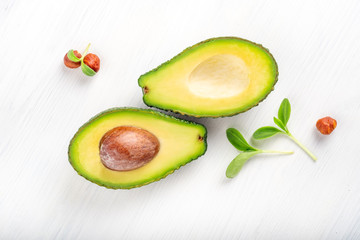 Ripe avocado cut into two parts on a white wooden background with nuts and leaves, one part with a bone.