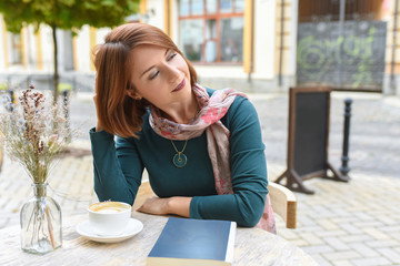 A young woman sits at a table in a summer cafe.