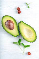 Ripe avocado cut into two parts on a white wooden background with nuts and leaves, one part with a bone.