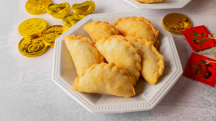 Chinese symbols on ornaments, red pockets and coins, means wealth. Tea setting with deep fried puff pockets, yau gok. Traditional Chinese New Year snack eating during celebration season.