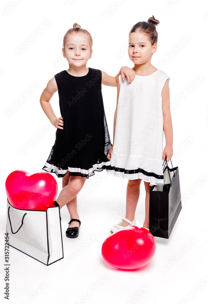 Wall mural 2 little girls with elegant dresses stay next to large bags with heart-shaped balloons inside