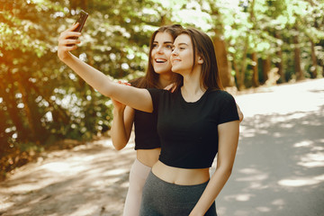 Beautiful sportsgirls in a summer forest. Ladies in a black top. Women use the phone