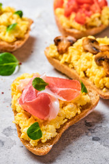 Scramble omelet sandwiches, bacon, mushrooms, tomatoes and fresh herbs on a light gray background.