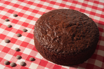 Chocolate sponge cake on a red and white tablecloth with pieces of chocolate