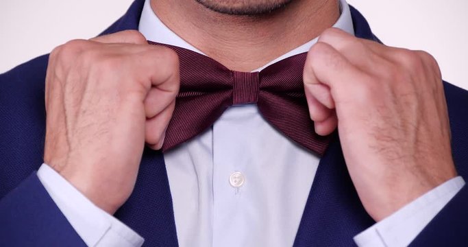 Man in elegant suit adjusting bow tie on white background, closeup