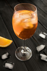 Aperol spritz cocktail in wine glass on the black wooden background. Location vertical. Closeup.