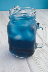 Iced blue flower tea in the glass on the white wooden background. Location vertical. Copy space. Closeup.