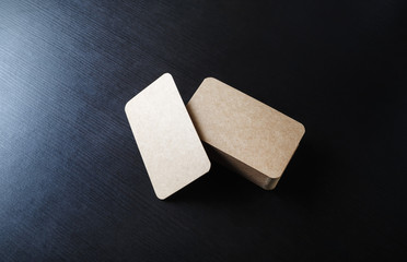Photo of blank kraft business cards on black wood table background. Template for branding ID.