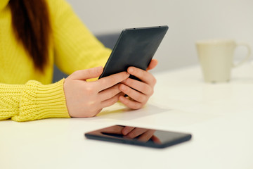 Close-up view of the arms of the caucasian woman holding an electronic book. Cell phone laying near on the table. Concept of the education, exam preparation, reading
