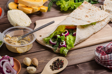 Shawarma with hummus, pumpkin, vegetables and salad on a dark wooden background with ingredients. Vegetarian food.