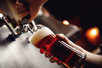 Bartender pours craft drink beer from tap into glass, dark background