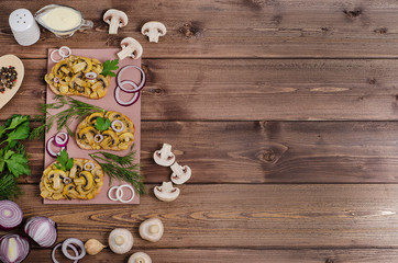 Sandwiches with fried champignons on a wooden board on a dark wooden background with ingredients and sauce with copy space. For advertising
