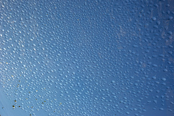 water drops on a glass pane with reflections and a blue background