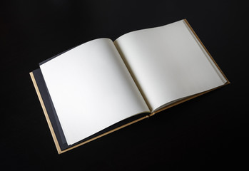 Open blank book on black wood table background.
