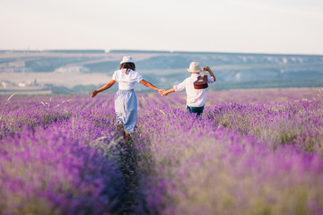 Boy and girl from the back in a lavender field and rustic clothes. They walk with a guitar and hold hands