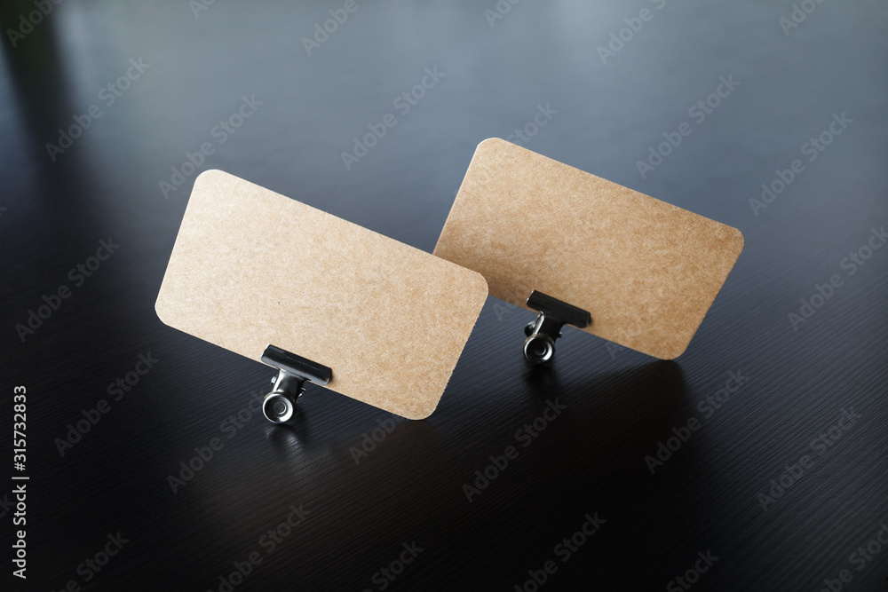 Wall mural photo of blank kraft business cards and metal binder clips on black wood table background.