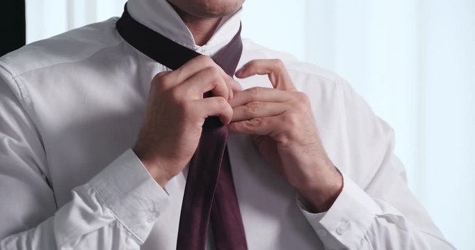 Man in elegant shirt tying tie indoors, closeup