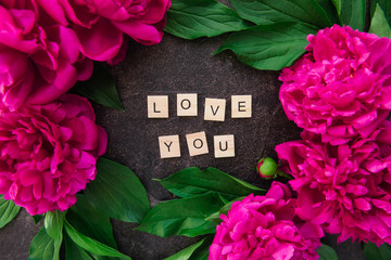Close up Love you text on wooden blocks border with the frame made of fresh pink peonies with green...