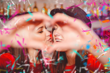 Two young lesbian girls kiss and make a heart with their hands at a club party.