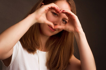 brunette showing love with hands in the shape of a heart, expressing a healthy symbol of the holiday Valentine's day