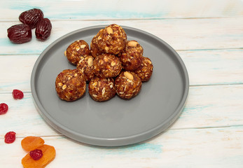 Homemade energy balls like a healthy breakfast or a snack of raisins, dried apricots, dates, nuts and oatmeal, that lie on  a gray ceramic plate on a white wood background. 