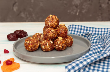 Homemade energy balls like a healthy breakfast or a snack of raisins, dried apricots, dates, nuts and oatmeal, that lie on  a gray ceramic plate on a white wood background and blue towel. 