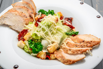 Caesar salad with croutons, quail eggs, cherry tomatoes and grilled chicken on a wooden background