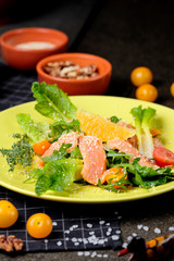 Cold salmon salad with green leaves, cucumber, avocado, lime and tomato on black stone background. Top view with copy space. Rustic style.