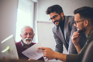 An employee showing charted report printed on a piece of paper to two businessmen in an office.