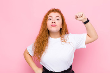 young red head woman feeling serious, strong and rebellious, raising fist up, protesting or...